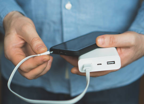 Person connecting a smartphone to a white portable power bank, illustrating portable power bank usage.